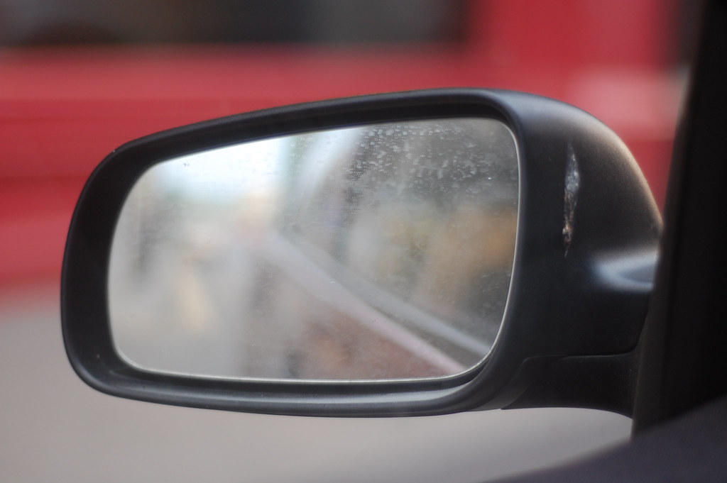 Close view of a car side mirror with a blurred road reflection