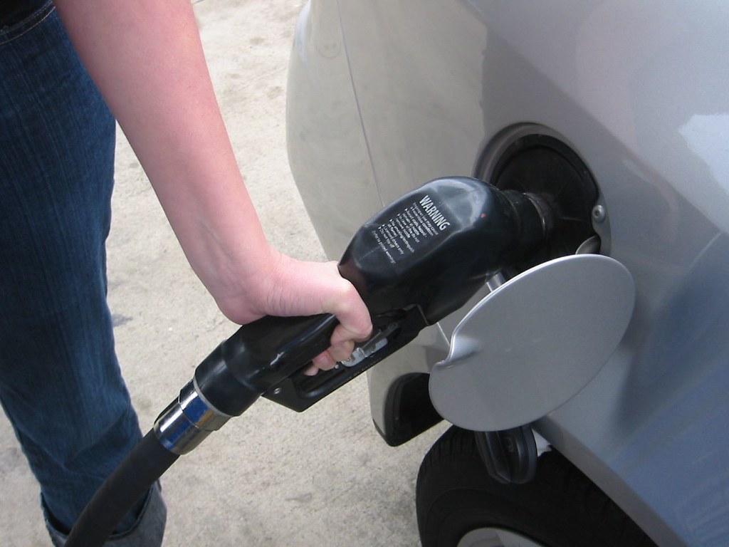 Hand holding a black fuel pump nozzle in a car fuel filler