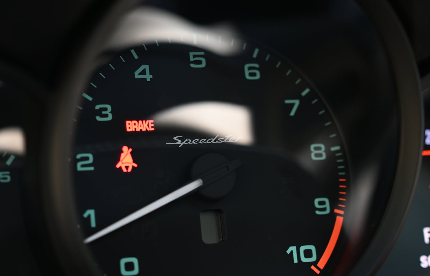 Red BRAKE warning word and seat belt icon on a car dashboard gauge