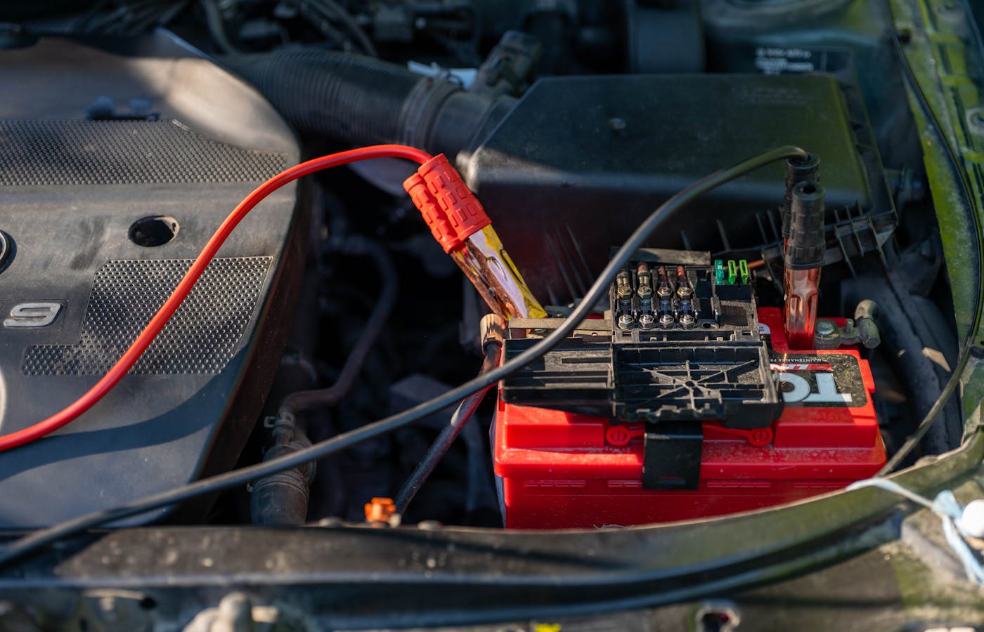 Car battery with jumper cables attached in an engine bay