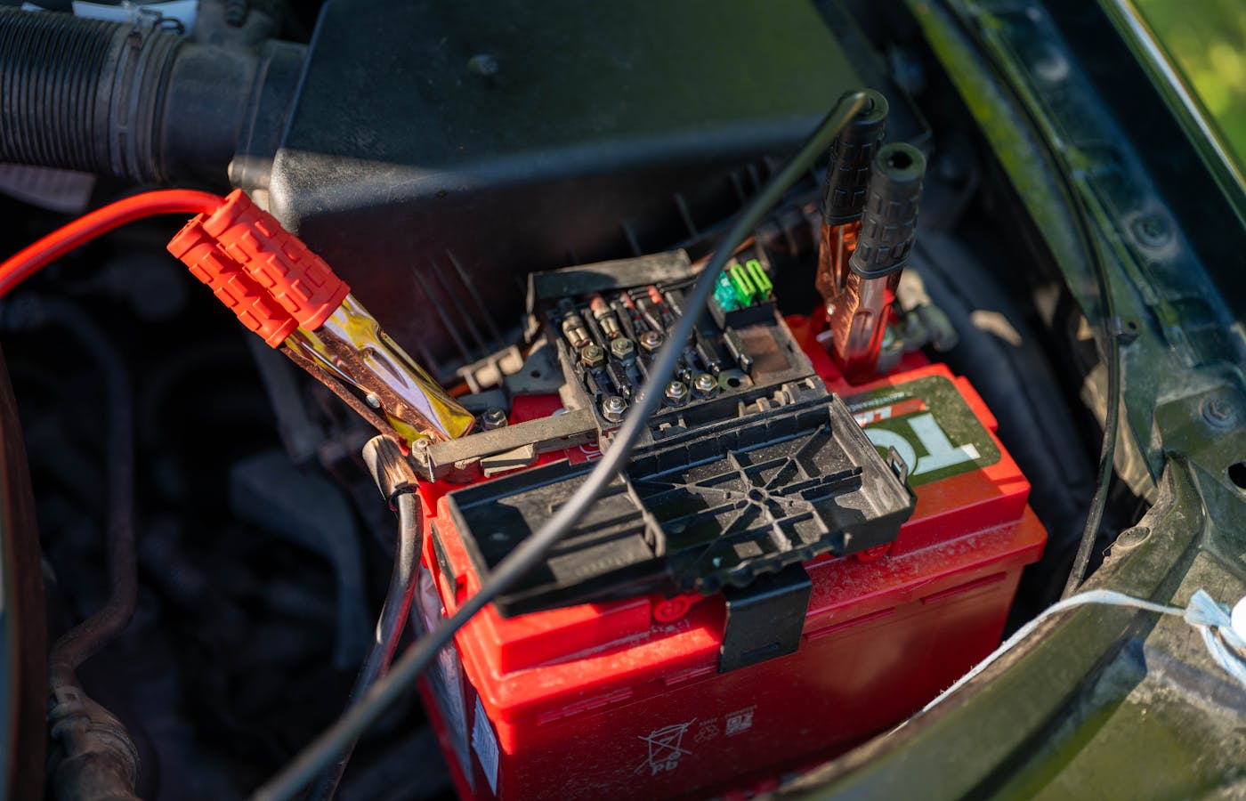 Car battery with jumper cables attached in an engine bay