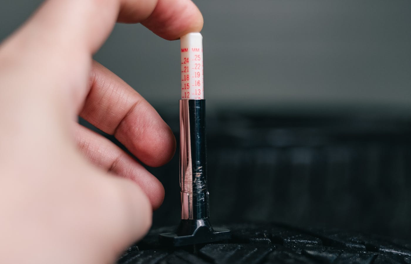 Hand holding a tread depth gauge on a car tire