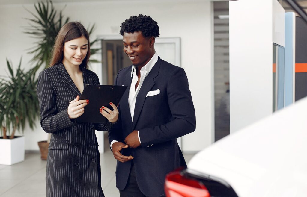 Two people reading a clipboard beside a car in a dealership