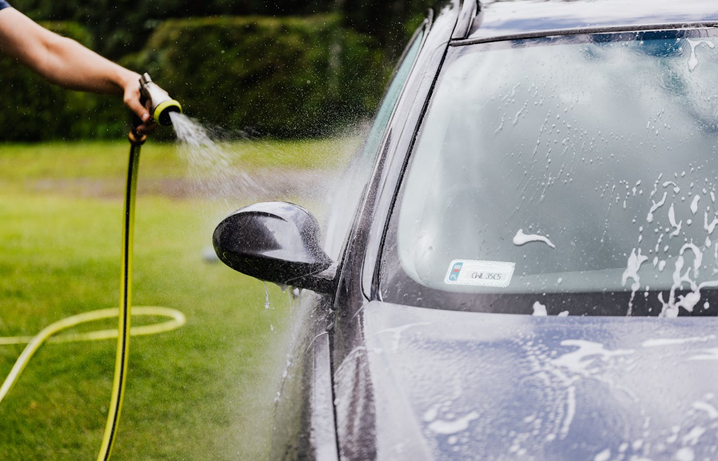 Person spraying water on a soapy car windshield
