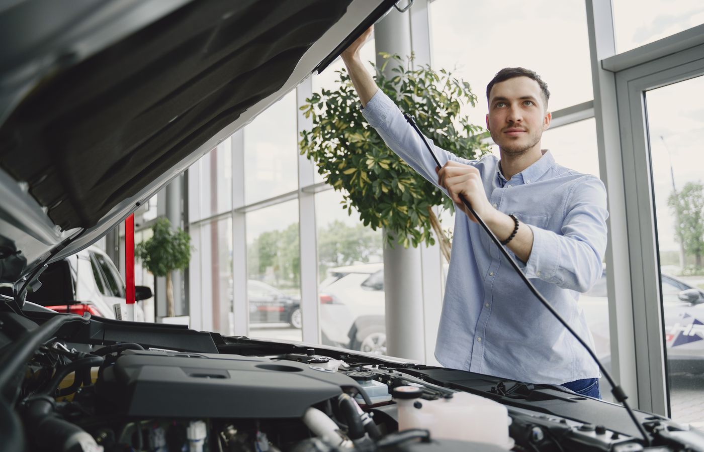 Person holding open a car hood to inspect the engine bay