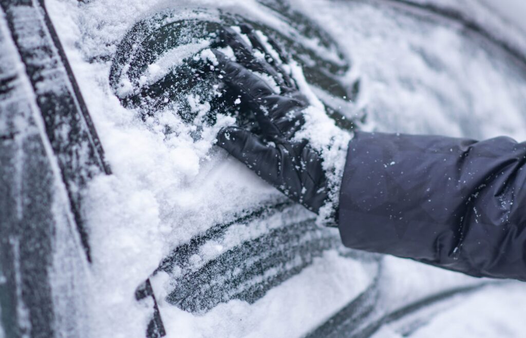 Gloved hand wiping snow from a car window