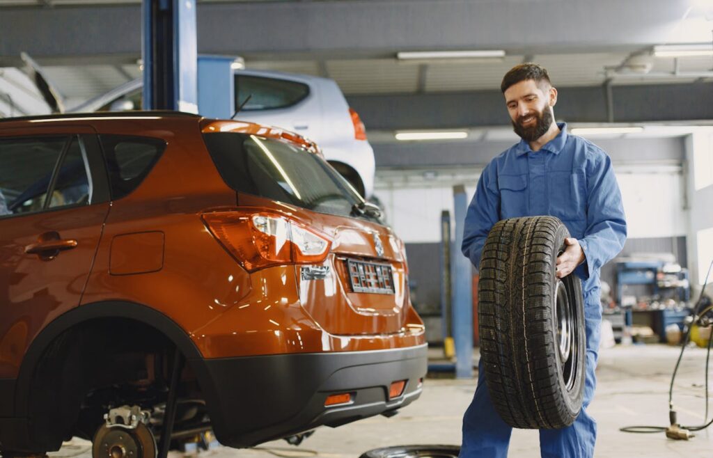 Mechanic holding a tire beside an orange car in a garage