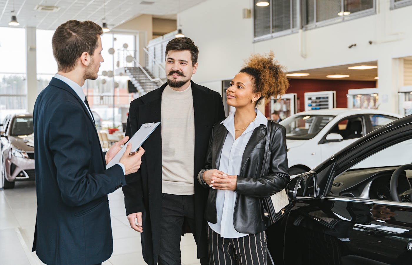 Salesperson speaking with two customers beside cars in a dealership