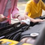 Person checking a car oil dipstick over an open engine bay