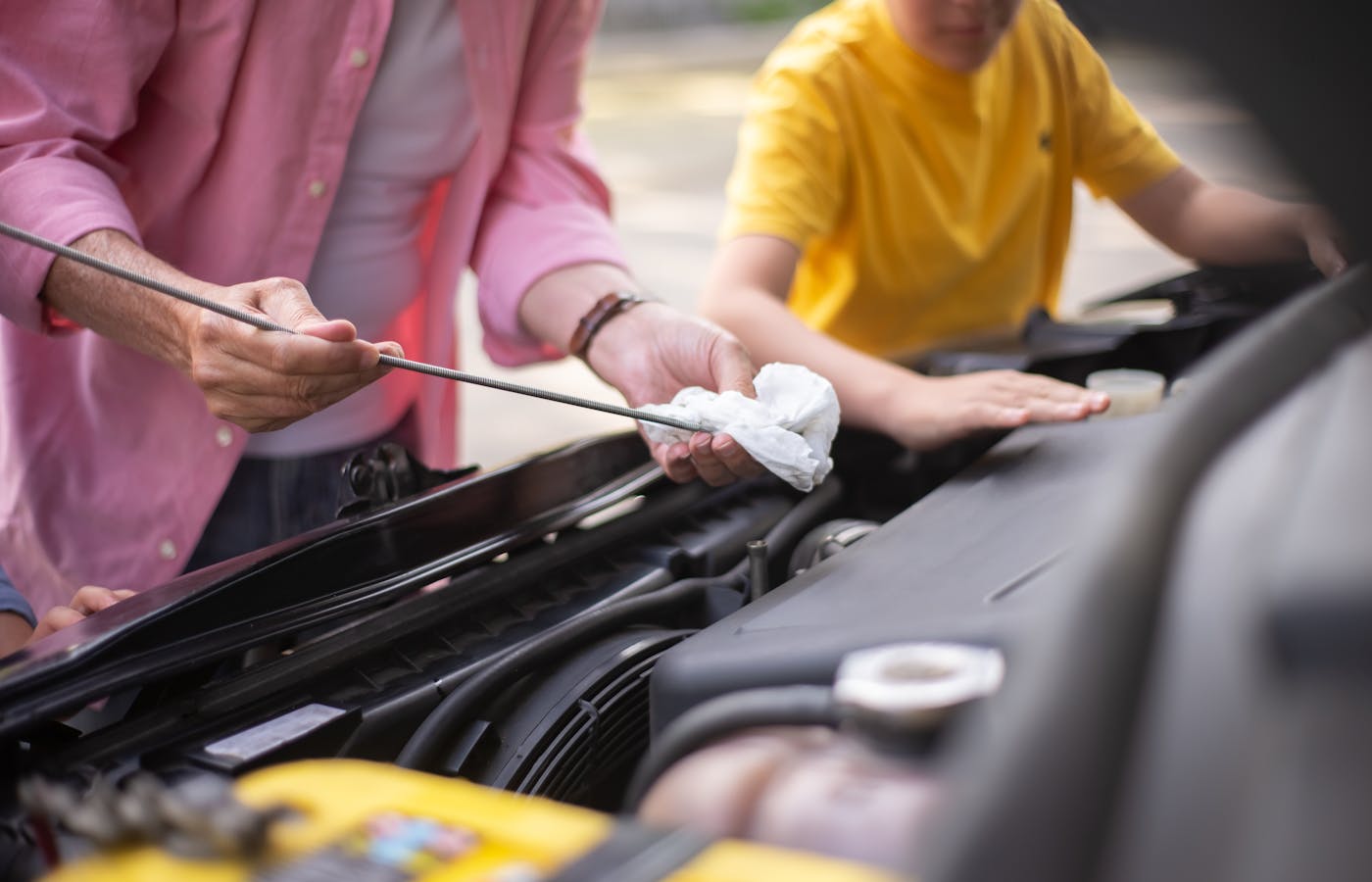 Person checking a car oil dipstick over an open engine bay