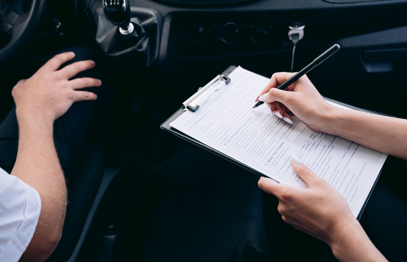 Person writing on a form while sitting inside a car