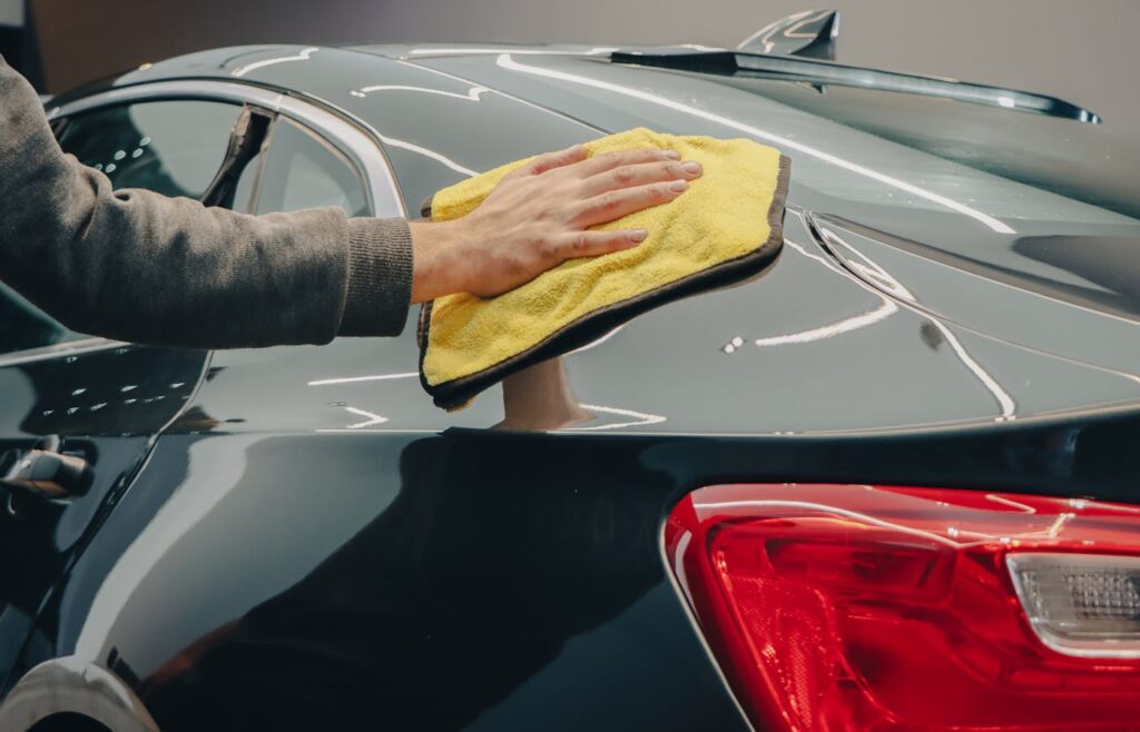 Hand wiping a car exterior panel with a yellow microfiber cloth