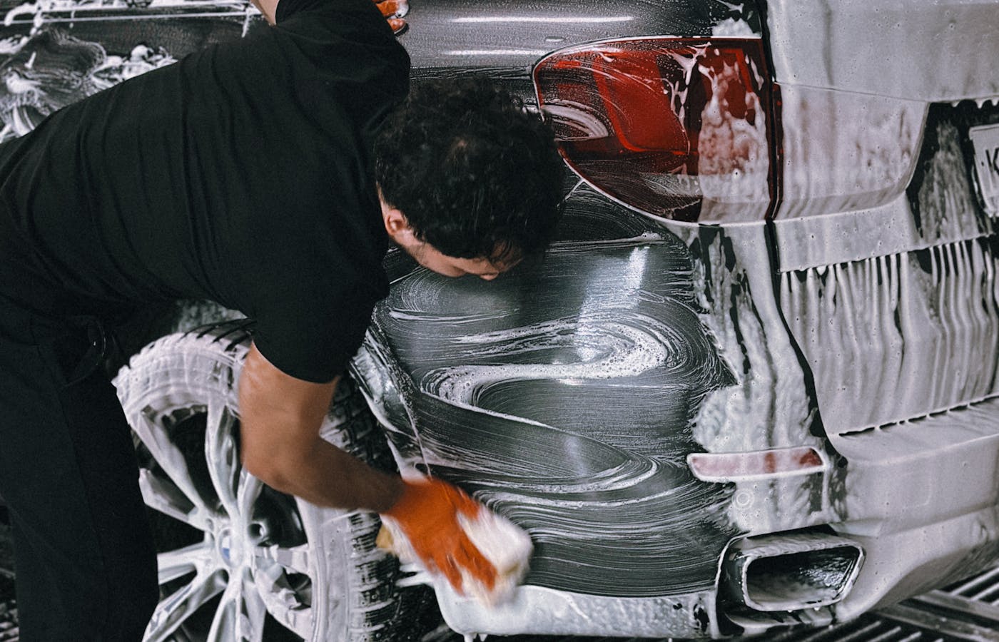 Person washing the rear side of a car with soap