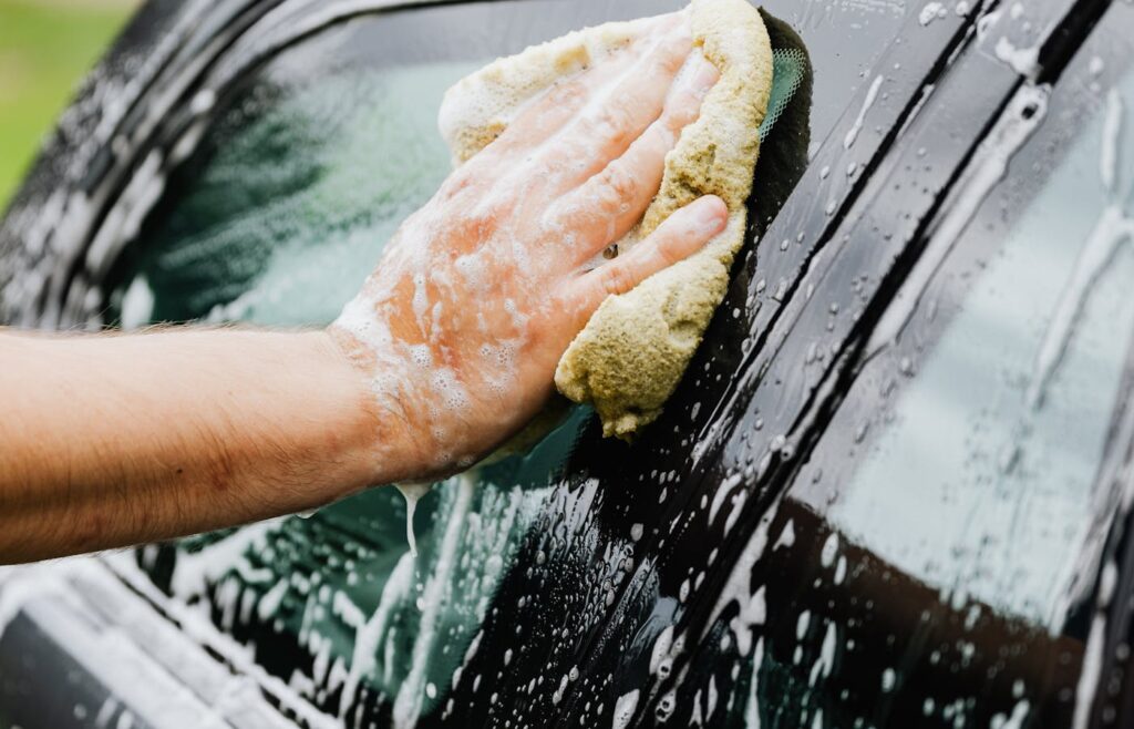 Person washing a car window with soap and sponge