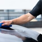 Hand wiping a car surface with a blue cloth