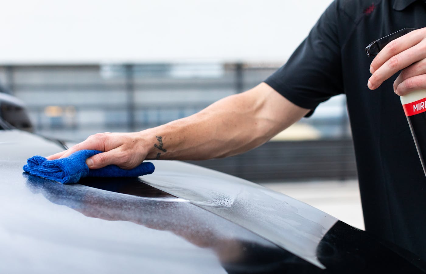 Hand wiping a car surface with a blue cloth